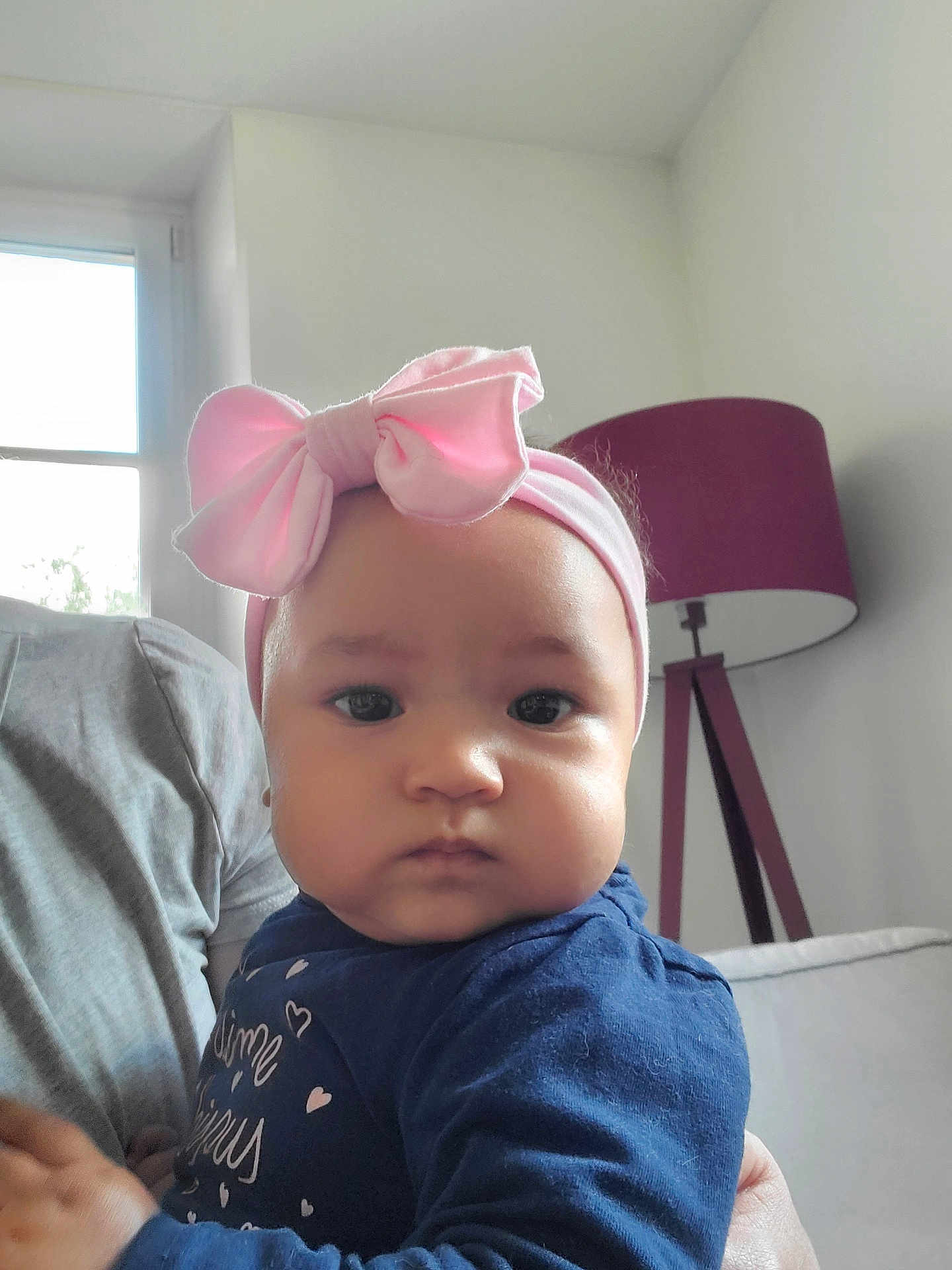 Nanisca participe au concours pour gagner de l'argent avec cette photo : baby, child, headband, pink_bow, face, indoor, lamp, person, portrait, blue_clothing, window, light, couch, adult_hand, expressionless, infant, closeup, human, sitting, home