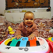 Nanisca a rejoint le concours — aidez-le/la à gagner de superbes lots ! baby, smiling, toy, piano, colorful, bed, blanket, tapestry, indoor, child, happy, playing, furniture, head, person, clothing, couch, cute, infant, room