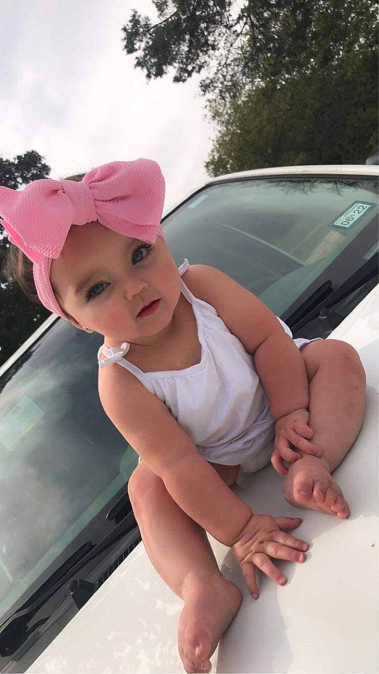 Brynley is registered to the contest to win money with this photo: automotive_design, automotive_exterior, automotive_lighting, bumper, cap, car, dress, finger, hairstyle, hand, hat, headwear, hood, motor_vehicle, person, plant, skin, sky, sun_hat, toddler