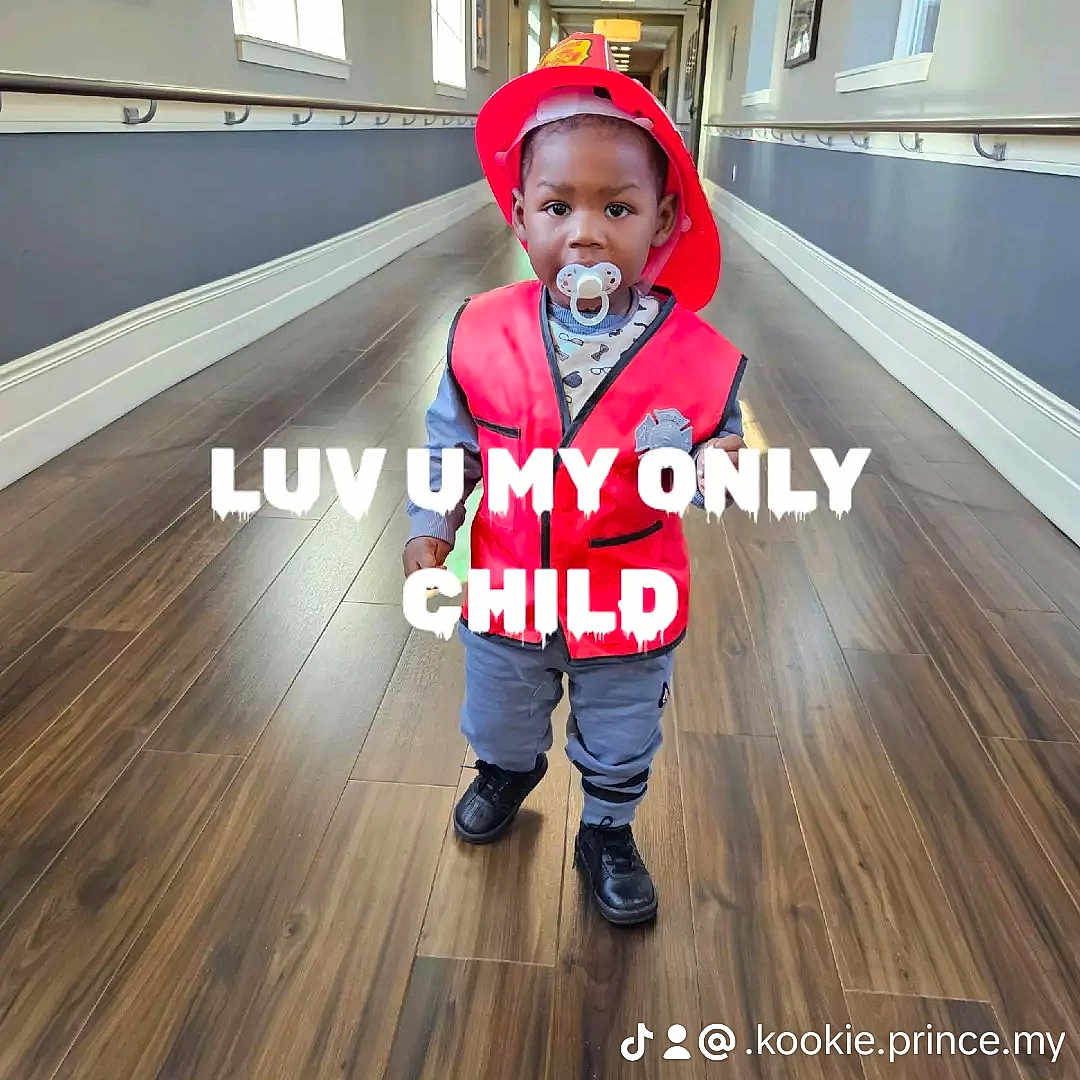 Prince is registered to the contest to win money with this photo: toddler, child, firefighter_costume, red_helmet, red_vest, pacifier, hallway, wooden_floor, windows, indoor, person, cute, standing, baby, floor, clothing, smile, young_child, portrait, costume