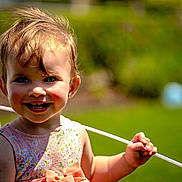 Willow is registered to the contest to win money with this photo: toddler, child, smiling, balloon, outdoor, greenery, sunlight, happy, face, portrait, dress, flower_pattern, rosy_cheeks, grass, nature, daylight, holding, cute, young_child, summer