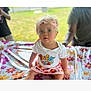 Delilah is registered to the contest to win money with this photo: toddler, child, outdoor, tablecloth, floral_pattern, colorful_clothing, headband, blue_eyes, person, sitting, curious, innocent, summer, daylight, adult_blur, grass, nature, casual, portrait, cute