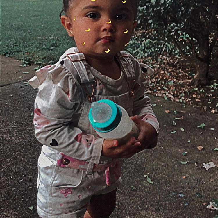 Charlette joined the competition — help win amazing prizes! bottle, buildings, bushes, casual_clothing, child, crescent_moon, cute, daylight, face_stickers, grass, outdoor, overalls, person, playful, sidewalk, sneakers, standing, toddler, trees, young_child