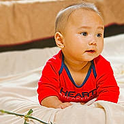 Kyrie joined the competition — help win amazing prizes! baby, infant, red_clothing, blanket, flower, indoor, portrait, cute, child, lying_down, soft_texture, curious, face, head, skin, hand, young_child, expression, cozy, casual