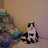 Gus is registered to the contest to win money with this photo: cat, kitten, black_and_white, sitting, bed, doll, toy, stuffed_toy, bedroom, indoors, furniture, blanket, pillow, wall, portrait, pet, animal, whiskers, ears, home_decor