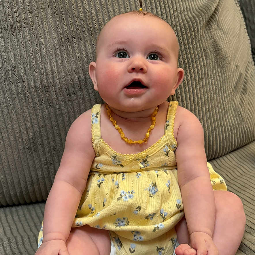 Drixley Dream is registered to the contest to win money with this photo: amber_beads, baby, barefoot, child, couch, cushion, cute, drooling, floral_pattern, hands, indoor, infant, necklace, portrait, rosy_cheeks, sitting, sofa, soft_texture, toes, yellow_dress