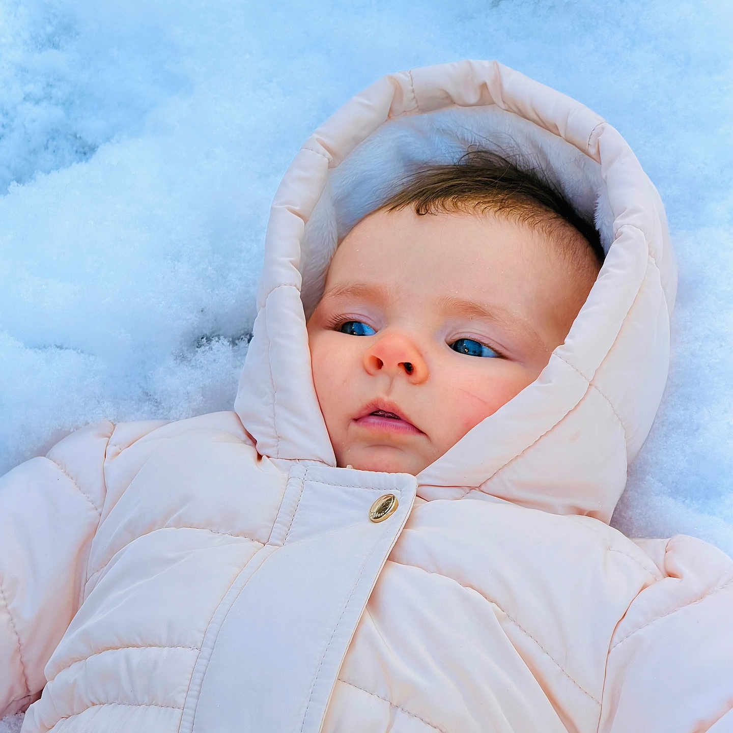 Mia participe au concours pour gagner de l'argent avec cette photo : baby, blue_eyes, cheeks, child, cold, expression, face, hood, infant, lying_down, nature, outdoor, pale_pink, skin, snow, snowsuit, soft, warm, winter, winter_clothing