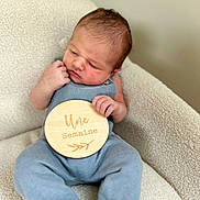 Simon a rejoint le concours — aidez-le/la à gagner de superbes lots ! baby, newborn, infant, blue_outfit, plaque, wooden_sign, one_week, sitting, chair, soft_texture, cozy, portrait, cute, indoors, child, face, hands, feet, skin, expression