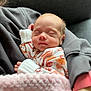 baby, newborn, sleeping, blanket, onesie, patterned_clothing, person, arm, sleeve, cozy, soft_texture, indoor, closeup, face, peaceful, infant, rest, cuddle, comfort, warmth
