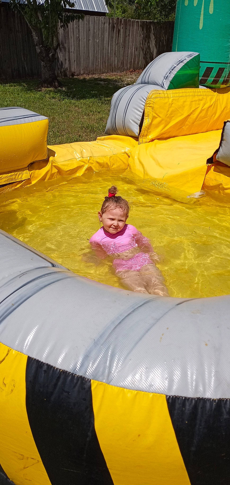 Lily-ann is registered to the contest to win money with this photo: automotive_exterior, comfort, event, fun, games, grass, inflatable, leisure, light, magenta, motor_vehicle, outdoor_play_equipment, person, plant, play, recreation, shade, smile, t_shirt, toddler
