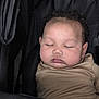 baby, sleeping, stroller, child, infant, cute, face, curly_hair, closed_eyes, peaceful, beige_clothing, chubby_cheeks, portrait, resting, indoors, black_fabric, soft_lighting, young_child, cozy, toddler