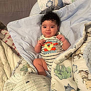 Ezekiel a rejoint le concours — aidez-le/la à gagner de superbes lots ! baby, child, blanket, bed, clothing, cute, face, funny_text, happy, indoor, infant, person, portrait, smile, striped_clothing, toddler, toy_pattern, warm, wrapped, young