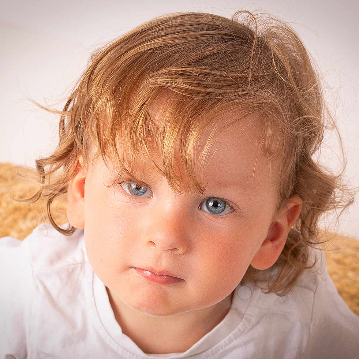 Léo participe au concours pour gagner de l'argent avec cette photo : blue_eyes, casual_clothing, child, close_up, curly_hair, cute, expression, face, head_and_shoulders, indoor, looking_at_camera, natural_light, person, portrait, skin, soft_background, texture, toddler, white_shirt, young_child