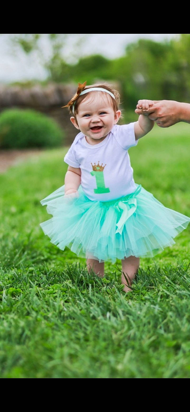 Sutton is registered to the contest to win money with this photo: baby, baby_toddler_clothing, child, event, face, fun, gesture, grass, grass_family, grassland, happy, joy, lawn, leisure, meadow, people_in_nature, person, pink, plant, recreation