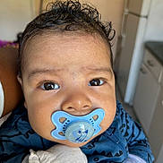 Angela joined the competition — help win amazing prizes! baby, infant, pacifier, blue_pacifier, close_up, face, eyes, curly_hair, onesie, mittens, hand, cheeks, portrait, indoor, kitchen_background, holding, cute, skin, expression, adorable