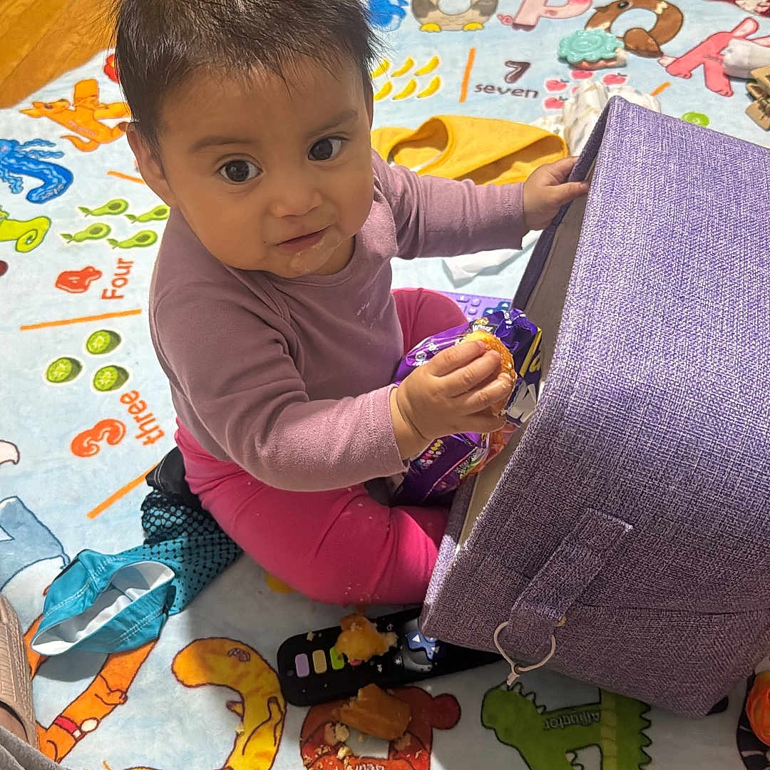 Ailany is registered to the contest to win money with this photo: baby, casual_clothing, child, colorful, curious, cushion, eyes, face, hardwood_floor, home, indoor, infant, play_mat, playtime, portrait, rug, sitting, smiling, snack_bag, toy