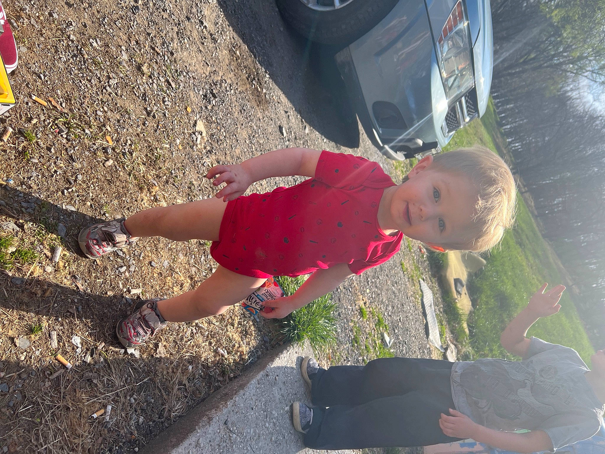 Aiden is registered to the contest to win money with this photo: asphalt, automotive_lighting, automotive_tire, car, fun, grass, human_leg, leg, leisure, light, people_in_nature, person, plant, recreation, tire, toddler, tree, vehicle, vehicle_door, water