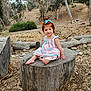Andrea joined the competition — help win amazing prizes! toddler, child, outdoor, tree_stump, dress, barefoot, nature, wooded_area, smile, bow, hair_accessory, playful, sitting, young_child, casual, daylight, trees, leaves, rocks, ground