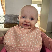 Saylor joined the competition — help win amazing prizes! baby, bib, child, clock, clothing, cute, face, furniture, happy, home, indoor, infant, light, person, pink, portrait, seat, sitting, smile, wall