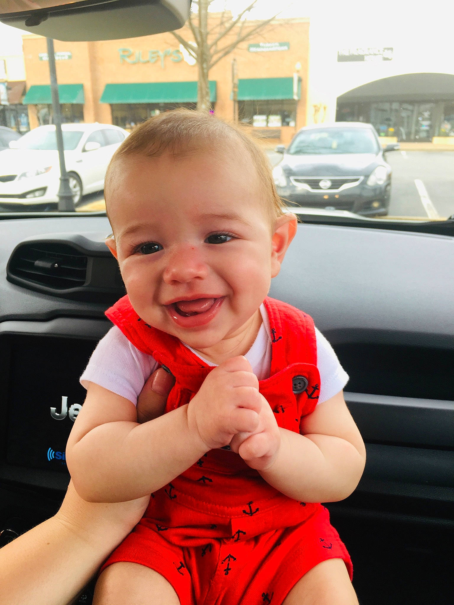 Sullivan is registered to the contest to win money with this photo: arm, baby, car, car_seat, cheek, child, chin, face, facial_expression, finger, hand, joy, person, product, red, skin, smile, thumb, toddler, vacation