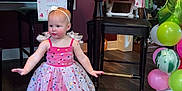 Ivy joined the competition — help win amazing prizes! toddler, child, birthday_party, dress, barefoot, balloons, high_chair, wooden_floor, decorations, sign, headband, pink, colorful, celebration, indoor, furniture, table, chair, party, smiling