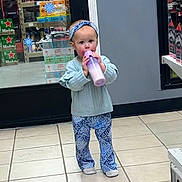 Ivy is registered to the contest to win money with this photo: toddler, child, bottle, drinking, headband, blue_clothing, patterned_pants, indoors, store, beverages, floor_tiles, sneakers, person, shopping, aisle, shelf, glass_door, casual, cute, standing