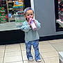 toddler, child, bottle, drinking, headband, blue_clothing, patterned_pants, indoors, store, beverages, floor_tiles, sneakers, person, shopping, aisle, shelf, glass_door, casual, cute, standing
