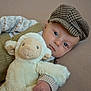 baby, child, plush_toy, sheep, hat, knitted_clothing, couch, soft_toy, indoor, portrait, cute, infant, face, hand, cozy, relaxing, looking_at_camera, neutral_expression, fabric, comfort