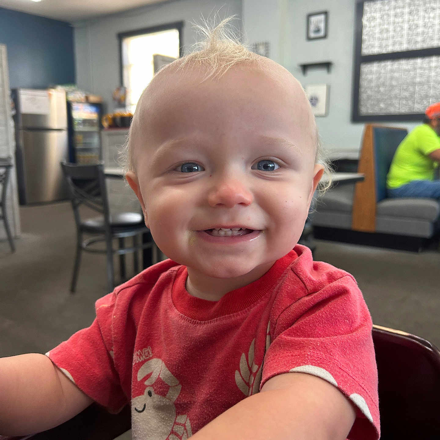 Caspian joined the competition — help win amazing prizes! background_people, blond_hair, blue_eyes, casual_clothing, chair, child, cute, dining_area, face, happy, high_chair, indoor, light, person, portrait, red_shirt, smiling, table, toddler, window