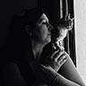 woman, person, cat, pet, portrait, black_and_white, window, indoor, sitting, profile, face, hands, arms, shoulder, dramatic_lighting, natural_light, silhouette, whiskers, feline, companionship