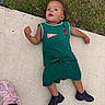 bare_arms, casual, child, concrete, curly_hair, daytime, footwear, grass, green_clothing, lying_down, outdoor, person, playing, relaxed, sidewalk, sneakers, sportswear, summer, toddler, young_child