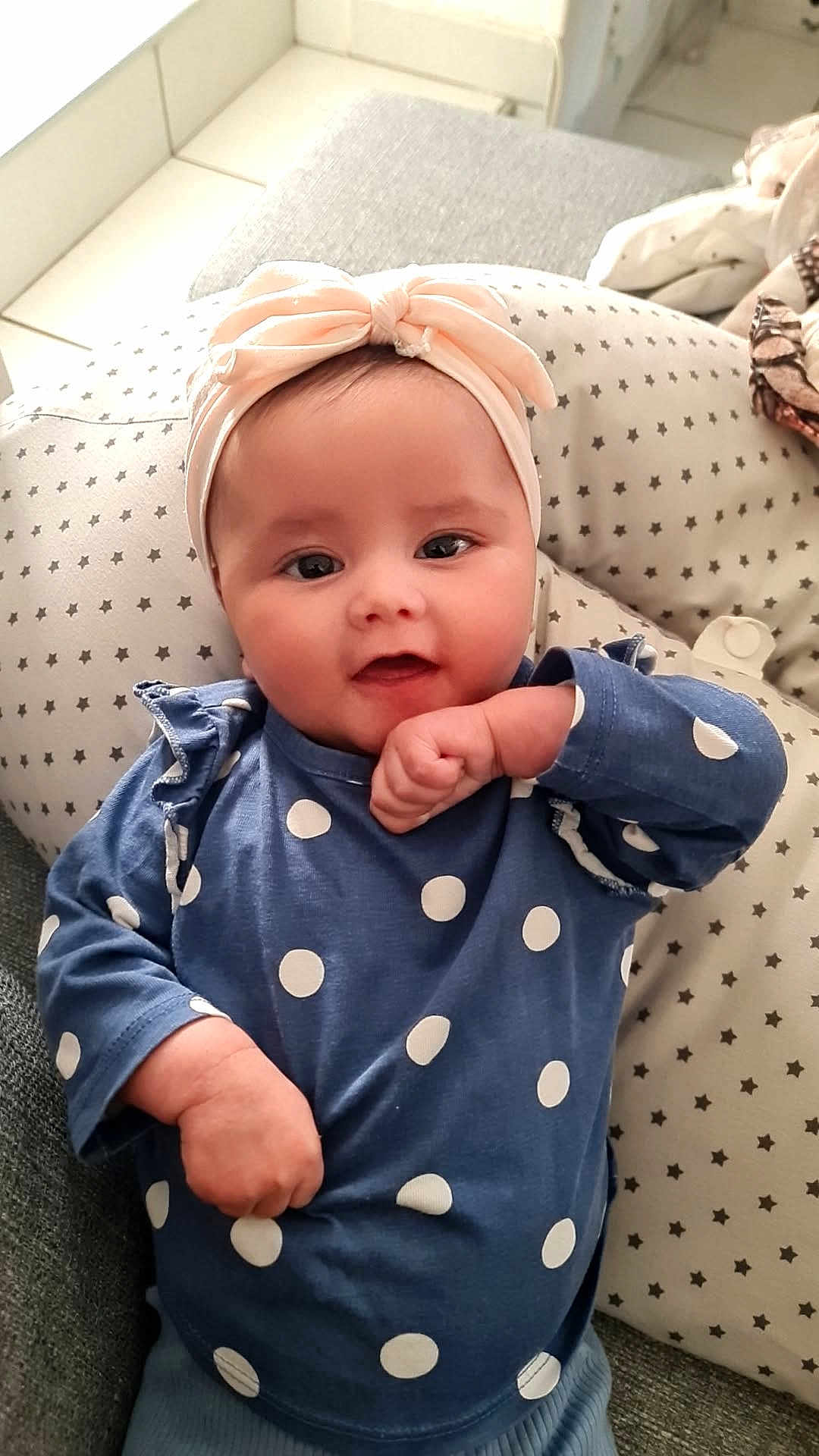 Dina a rejoint le concours — aidez-le/la à gagner de superbes lots ! baby, infant, child, headband, bow, polka_dot, blue_shirt, cushion, star_pattern, smile, fist, indoor, cozy, cute, portrait, person, happy, soft_lighting, seated, comfortable
