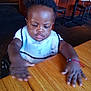 Moses joined the competition — help win amazing prizes! baby, child, infant, toddler, portrait, highchair, wooden_table, restaurant, indoor, curly_hair, dark_skin, bib, hands, motion_blur, furniture, chair, table, dining, expression, cute