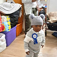 Moses joined the competition — help win amazing prizes! adult, bag, blue_ribbon, casual, child, clothing, cozy, curious, floor, furniture, hat, home, indoor, person, phone, pom_poms, socks, standing, toddler, wooden_floor