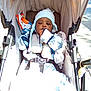 baby, child, stroller, carriage, canopy, blanket, earflap_hat, hat, mittens, snack_bag, chips, harness, buckle, seat, outdoor, sidewalk, pavement, portrait, cozy, relaxed