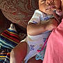 baby, sleeping, pacifier, blanket, cushion, patterned_fabric, infant, clothing, comfort, rest, colorful, soft, peaceful, person, indoors, closeup, skin, hand, foot, nap