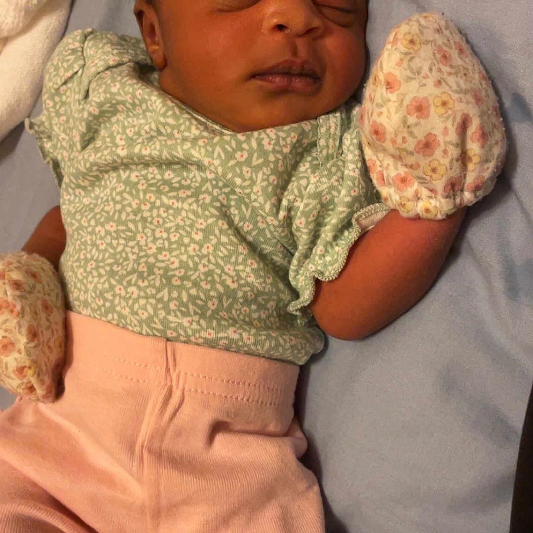 Denver Stallings is registered to the contest to win money with this photo: baby, bed, blanket, child, clothing, cute, floral_pattern, green_top, headband, indoors, infant, lying_down, mittens, newborn, peaceful, pink_pants, portrait, resting, sleeping, soft_light