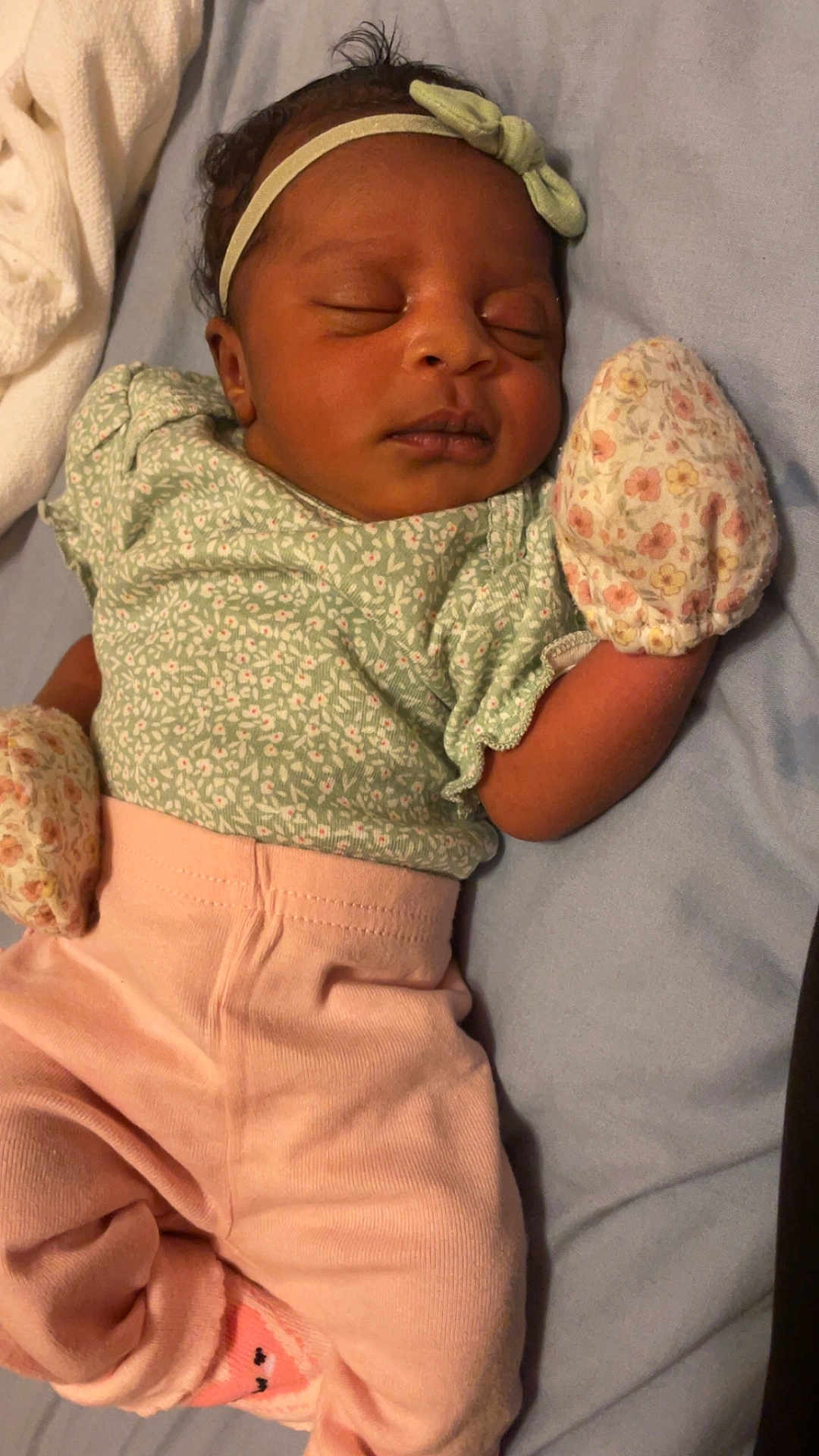 Denver Stallings is registered to the contest to win money with this photo: baby, sleeping, infant, headband, mittens, pink_pants, green_top, floral_pattern, blanket, bed, peaceful, cute, clothing, newborn, lying_down, indoors, soft_light, portrait, child, resting