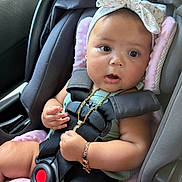 America is registered to the contest to win money with this photo: baby, car_seat, child, infant, headband, bow, straps, safety, pink_padding, gold_necklace, bracelet, curious, seated, indoors, car_interior, closeup, cute, young, person, portrait