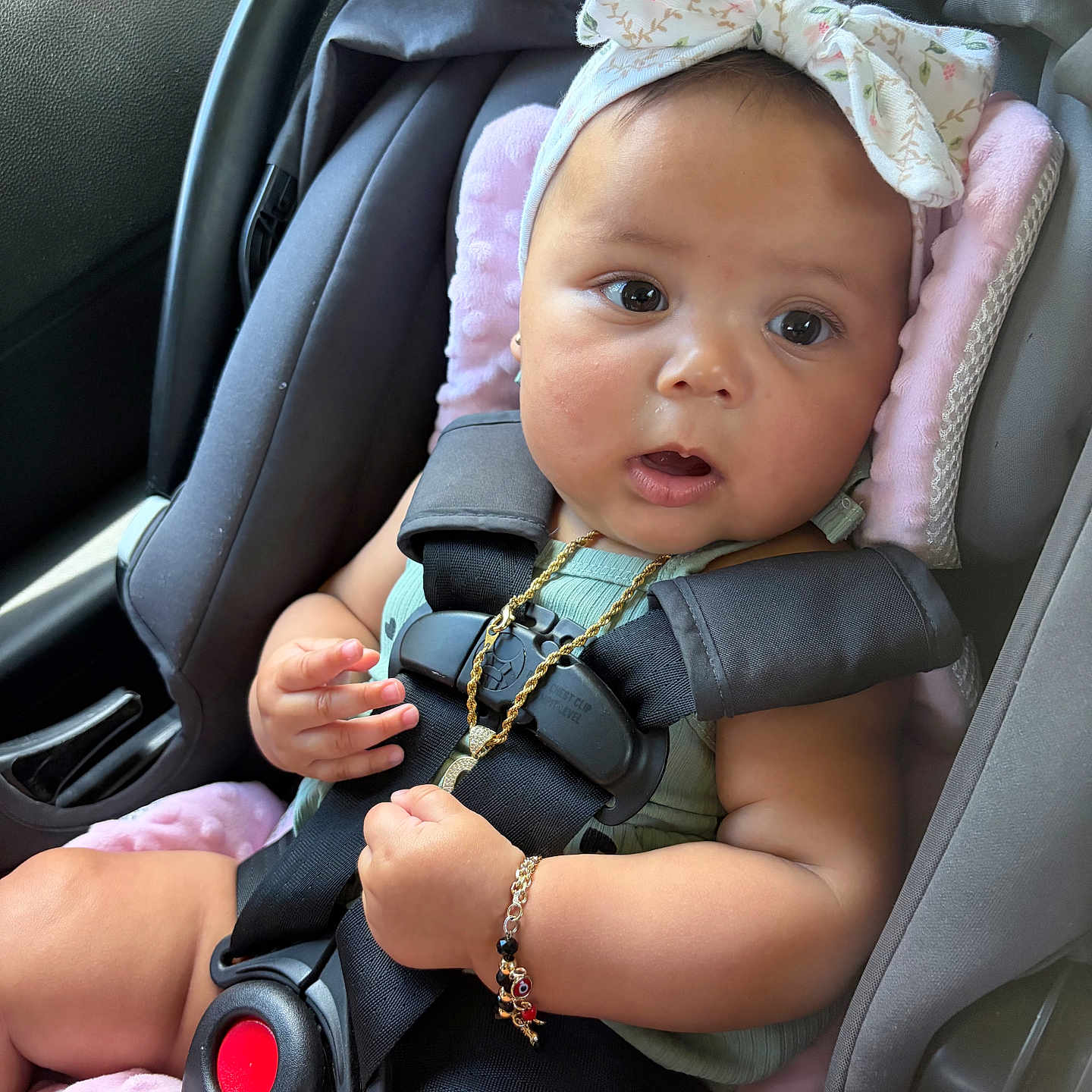 America is registered to the contest to win money with this photo: baby, car_seat, child, infant, headband, bow, straps, safety, pink_padding, gold_necklace, bracelet, curious, seated, indoors, car_interior, closeup, cute, young, person, portrait