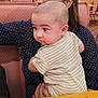 Adrian is registered to the contest to win money with this photo: baby, child, striped_clothing, polka_dot, person, indoor, restaurant, booth, table, seat, holding, curious, head, hair, face, adult, hands, furniture, pattern, casual