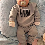 Eduardo is registered to the contest to win money with this photo: baby, pacifier, mitten, hat, sweatshirt, pants, socks, nba_logo, blanket, soft_fabric, indoor, infant, comfortable, cute, clothing, person, child, relaxed, lying_down, cozy
