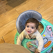 Lucas is registered to the contest to win money with this photo: toddler, baby_walker, child, smiling, indoor, wooden_floor, toy, play, curious, person, happy, young_child, clothing, seat, pink, green, beige, activity_center, infant, cute