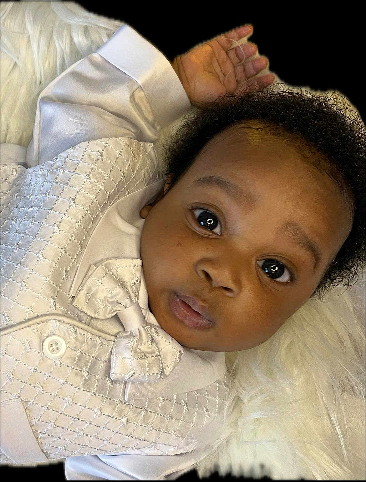David is registered to the contest to win money with this photo: baby, infant, white_clothing, bow_tie, curly_hair, face, eyes, hand, fluffy_background, portrait, closeup, cute, child, laying_down, soft_texture, skin, expression, elegant, young, person