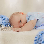 Kassandra is registered to the contest to win money with this photo: baby, infant, blue_outfit, rainbow_pattern, tiara, crown, blue_flowers, soft_surface, lying_down, cute, peaceful, portrait, child, small_hand, head, eyes, skin, sleepy, closeup, adorable
