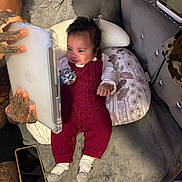 Zayan is registered to the contest to win money with this photo: baby, tablet, tattooed_hands, cushion, red_knit_outfit, socks, floral_pillow, sofa, blanket, wood_floor, person, indoor, technology, entertainment, hand, cute, child, comfort, home, relaxation