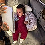 baby, tablet, tattooed_hands, cushion, red_knit_outfit, socks, floral_pillow, sofa, blanket, wood_floor, person, indoor, technology, entertainment, hand, cute, child, comfort, home, relaxation