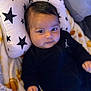 baby, infant, pillow, blanket, black_clothing, face, head, person, cute, indoors, star_pattern, soft_fabric, child, young, portrait, lying_down, comfort, warm, expression, cozy