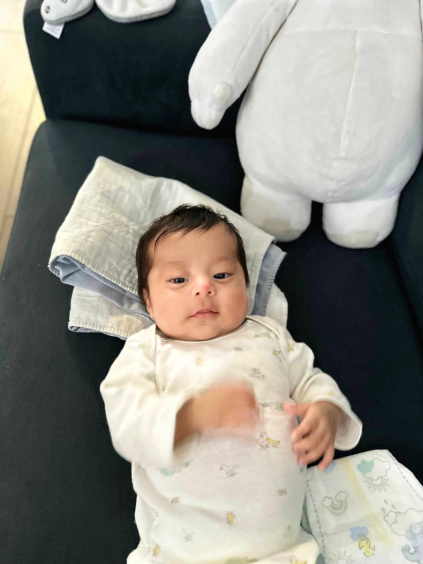 Olivia is registered to the contest to win money with this photo: baby, infant, onesie, stuffed_animal, couch, blanket, towel, diaper, indoor, child, person, cute, sleepwear, soft_toy, furniture, relaxing, lying_down, small_hands, face, calm