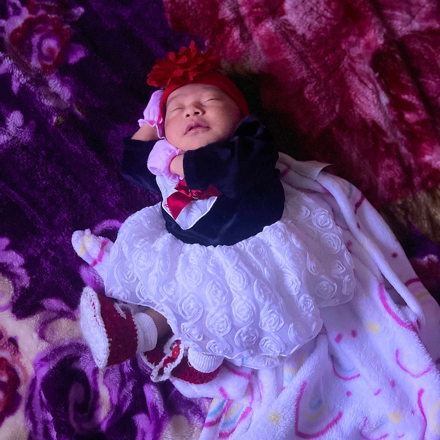 Dulce is registered to the contest to win money with this photo: baby, blanket, child, clothing, cozy, cute, dress, footwear, headband, indoors, infant, newborn, pattern, peaceful, purple, red, resting, sleeping, soft, white